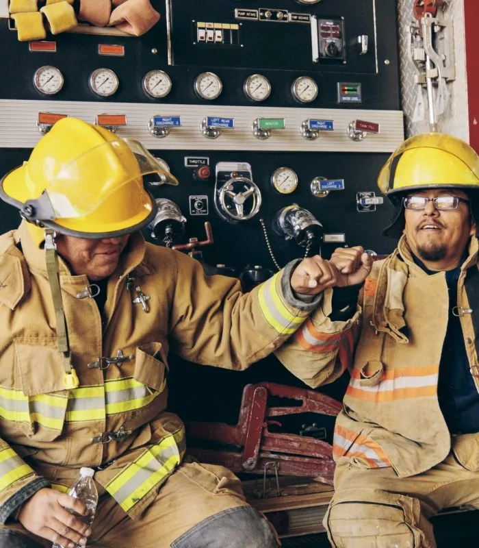 Two firefighters share a fist bump beside their engine.