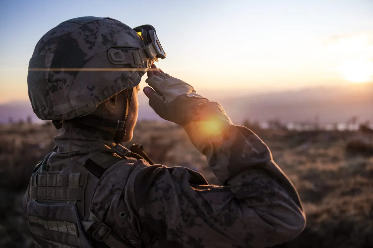 A uniformed service member saluting at sunset.